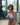 Woman in a blue bikini standing in a room with large windows and greenery outside.