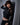 Woman in a black outfit posing against a gray curtain