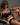 A highly realistic sex doll in a bikini sitting on a black bench.