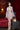 Realistic silicone doll in a white lace outfit standing in a room with red curtains and a lamp.