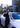 Woman in a black dress leaning against a white car with a cityscape background
