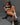 A highly realistic sex doll named Celeste, with long brown hair and a tan, is depicted sitting and holding a coffee cup. She is wearing a black and white sports crop top and leggings, exuding a sensual and health-focused aura.