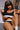 A highly realistic sex doll named Celeste, with long brown hair and a tan, is depicted sitting and holding a coffee cup. She is wearing a black and white sports crop top and leggings, exuding a sensual and health-focused aura.