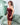 Woman in a red dress standing in a modern interior setting with a sofa and glass wall.