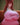 Person wearing a pink dress with a logo, sitting on a couch.