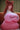 Person wearing a pink dress with a logo, sitting on a couch.