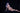 Naked person with blue hair and dark makeup sitting on a black surface against a black background