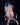 Statue of a nude figure with blue hair sitting on a chair against a black background