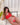 Person wearing a red lingerie set on a white couch with plants and curtains in the background.