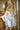 Sex doll wearing a white satin robe in a wooden room.