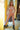 Naked mannequin with blonde hair and black boots in a room with yellow walls and a lamp.
