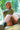 Realistic silicone doll with blonde hair and camouflage top sitting outdoors.