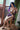 A sex doll with blue hair sitting on a chair near a window in a violet lingerie.