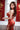 Woman in a red floral dress posing in front of a blurred background with Chinese characters.