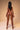 Naked person with braided hair sitting on a stool against a beige background