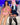 Two realistic sex dolls sitting next to each other, one wearing a pink-trimmed pink bikini and the other a schoolgirl outfit with blue and white stripes. Both dolls have long black hair and are made with a silicone head and body.