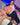 Two realistic sex dolls sitting next to each other, one wearing a pink-trimmed pink bikini and the other a schoolgirl outfit with blue and white stripes. Both dolls have long black hair and are made with a silicone head and body.