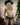 A realistic sex doll named Toriy, depicted wearing a white floral top and blue shorts, with long blonde hair styled with a black hat.