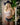 The image shows a highly realistic sex doll with long golden hair, wearing a pink lacey white top and a blue hat. The doll has a lifelike appearance with detailed facial features and is posed in a manner that highlights her natural curves.