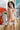 Partial topless person wearing a white garment with flowers and a painting in the background