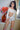 Woman in a white off-shoulder top and shorts standing indoors with flowers and a painting in the background.