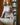 Woman in a beige ribbed sweater standing in a room with a bookshelf.