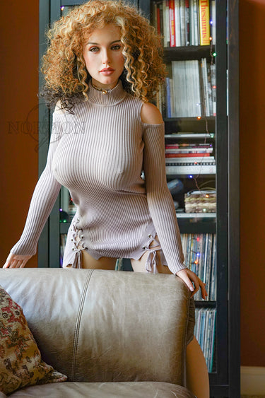 Woman in a beige ribbed sweater standing in a room with a bookshelf.