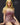 A highly realistic beige sex doll with long blonde hair, posed in a pink dress, sitting on a desk.