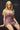 A highly realistic beige sex doll with long blonde hair, posed in a pink dress, sitting on a desk.