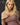 A highly realistic beige sex doll with long blonde hair, posed in a pink dress. The doll has a lifelike appearance with detailed facial features and a flexible skeleton, designed for versatile posing.
