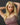 A highly realistic beige sex doll with long blonde hair, posed in a pink dress. The doll has a lifelike appearance with detailed facial features and a flexible skeleton, designed for versatile posing.