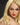 A highly realistic beige sex doll with long blonde hair, posed in a pink dress. The doll has a lifelike appearance with detailed facial features