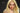 A highly realistic beige sex doll with long blonde hair, posed in a pink dress. The doll has a lifelike appearance with detailed facial features