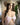 The image shows a highly realistic sex doll with long brown hair, wearing a pink lacey white top and a brown hat. The doll has a lifelike appearance with detailed facial features and is posed in a manner that highlights her natural curves.