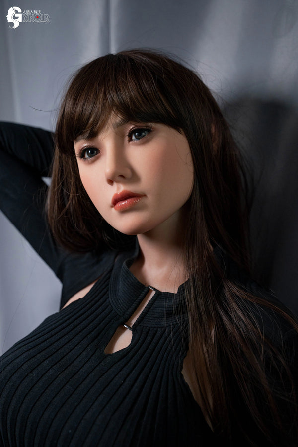 Realistic silicone doll with dark hair and black clothing against a neutral background