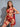 A woman wearing a red lingerie set with lace details and a G-string design, showing her curves.