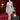 Realistic silicone doll in a white lace outfit standing in a room with red curtains and a lamp.