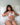Woman in white lace lingerie sitting on a bed with white pillows and bedding.