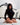 Woman in a black outfit sitting on a white bed with decorative headboard