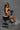 A highly realistic sex doll sitting on a black bench wearing gym wear.