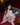 Sex doll in a white lace robe sitting on a red couch with a bottle of alcohol.