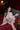 Sex doll in a white lace robe sitting on a red couch with a bottle of alcohol.