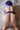 A sex doll with blue hair and violet lingerie showing her butt on a white bed.