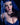Character with blue hair and costume against a dark background
