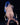 Statue of a nude figure with blue hair sitting on a chair against a black background