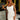 Woman in a white dress with braided hair standing in a bedroom setting.