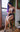 A sex doll with blue hair sitting on a chair near a window in a violet lingerie.