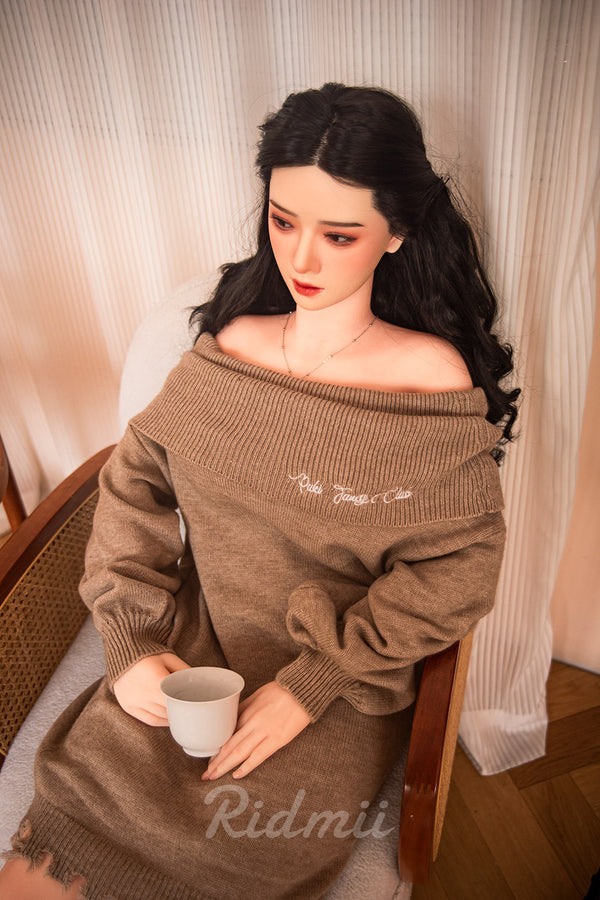 Person wearing a brown off-shoulder sweater with 'Ridmii' branding, holding a cup.