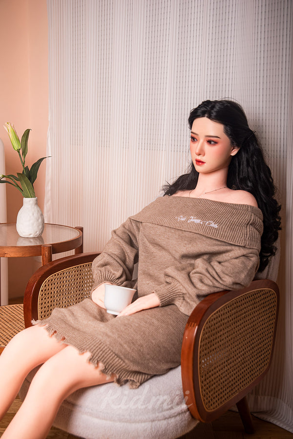 Person wearing a brown off-shoulder sweater sitting on a chair with a neutral background