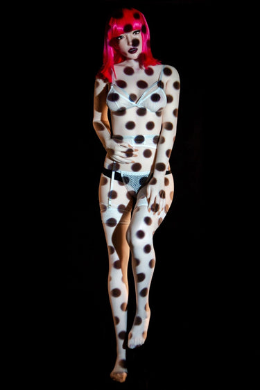 Person wearing a polka dot bodysuit and pink wig on a black background